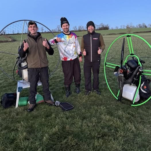 Three students standing in a field with paramotors, giving thumbs up.