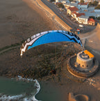 Person paramotoring near a coastal fort during sunset.