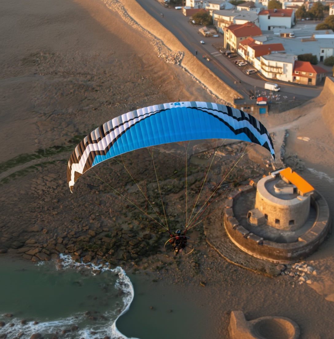 Person paramotoring near a coastal fort during sunset.