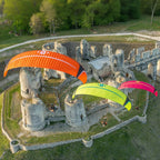Three Dudek solo 2 paramotors flying over an old castle ruins.